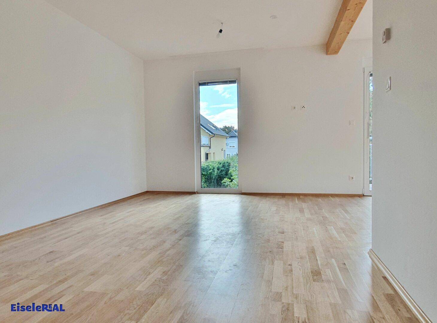 Heller Wohnbereich mit Parkettboden und hoher Fenstertür zum Garten oder Balkon.