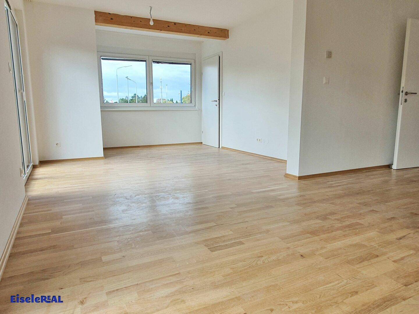 Geräumiger Wohnbereich mit hellem Parkettboden und großen Fenstern für viel Tageslicht.