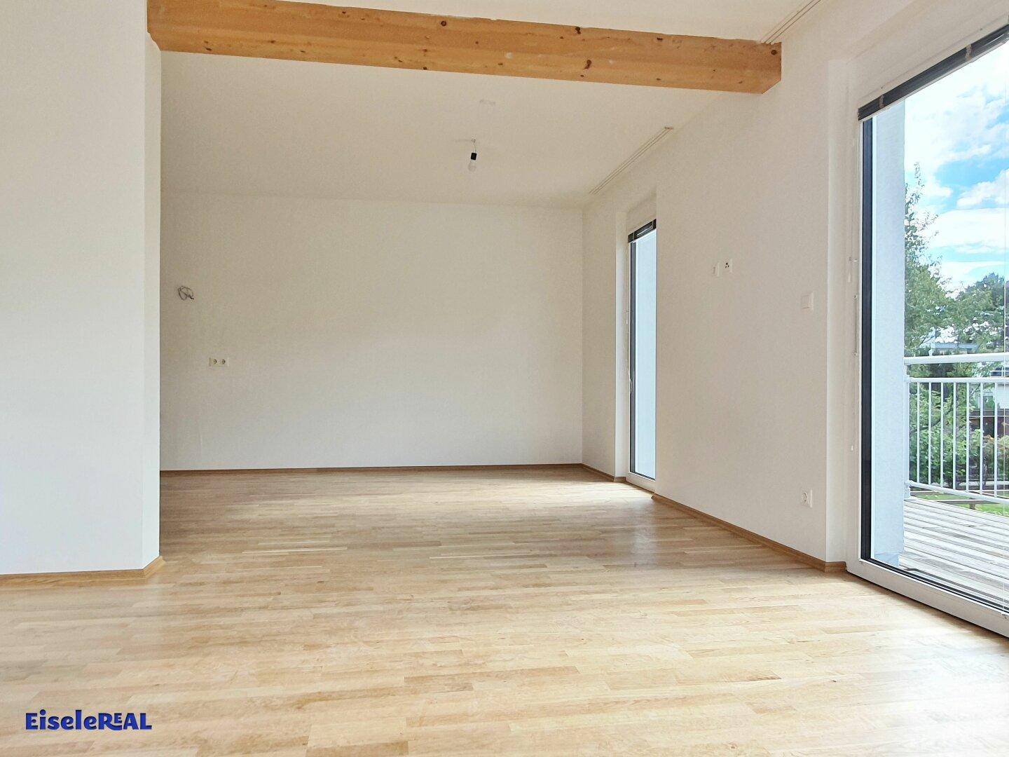 Lichtdurchfluteter Wohnbereich mit Holzbalken und Zugang zu einem Außenbereich.