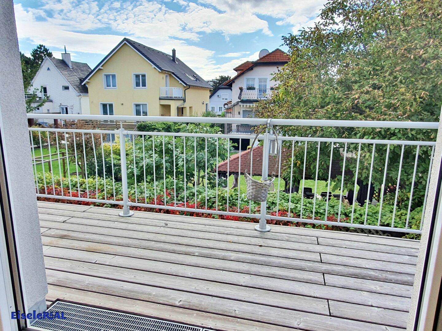Balkon mit Holzbelag und Blick auf den grünen Garten und die Nachbarschaft.