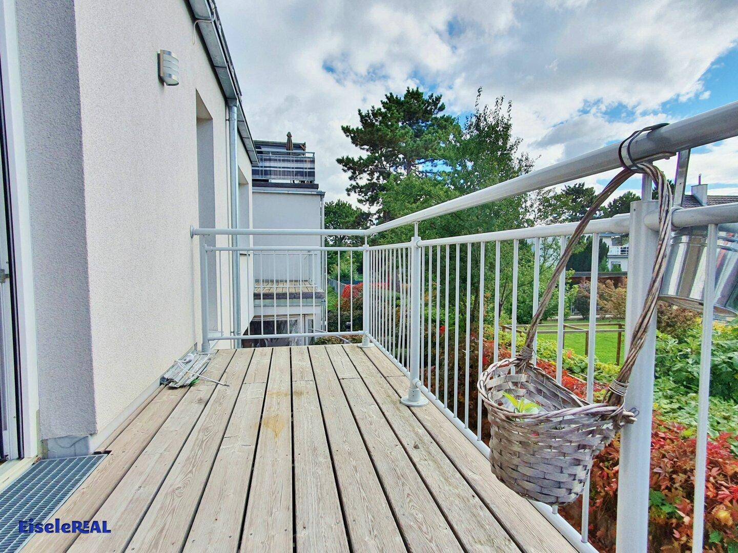 Gemütlicher Balkon mit Holzplanken und einem Korb, umgeben von viel Grün.