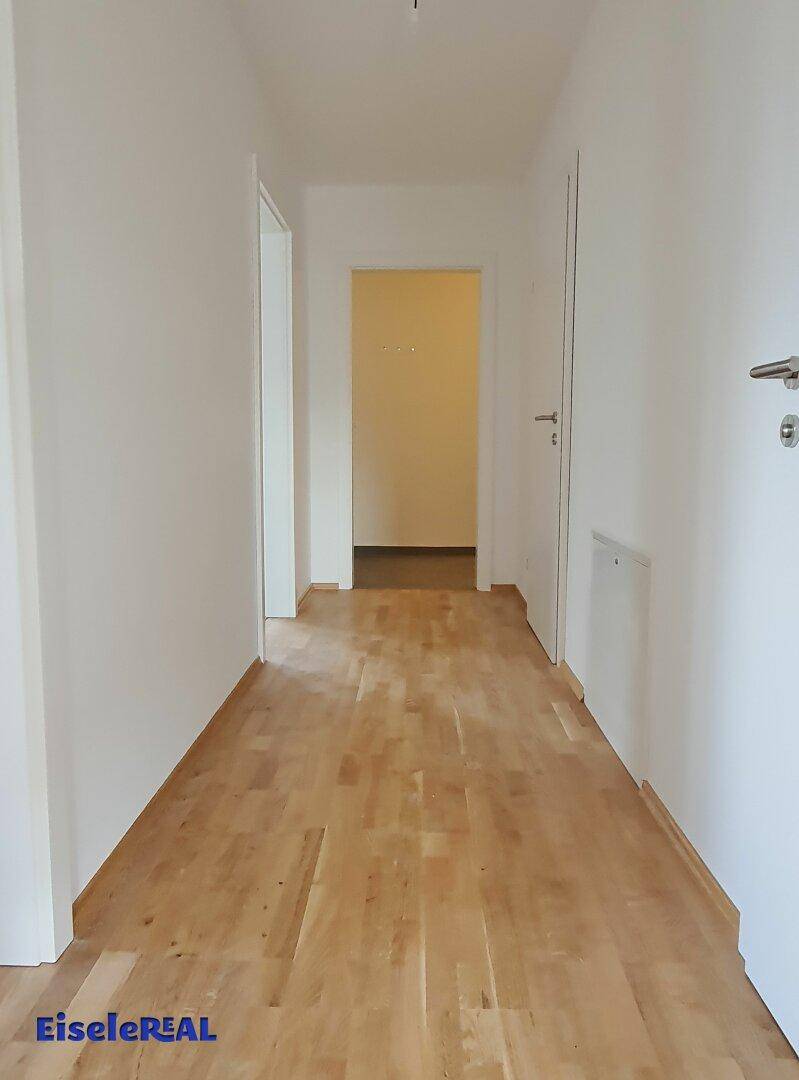 Langer Flur mit Parkettboden und weißen Wänden, der die Zimmer miteinander verbindet.