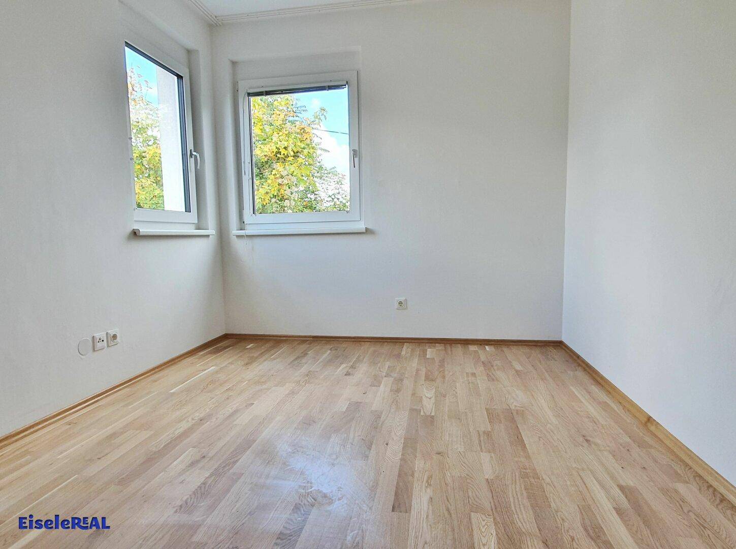 Helles Schlafzimmer mit Parkettboden und zwei Fenstern für gute Belichtung.