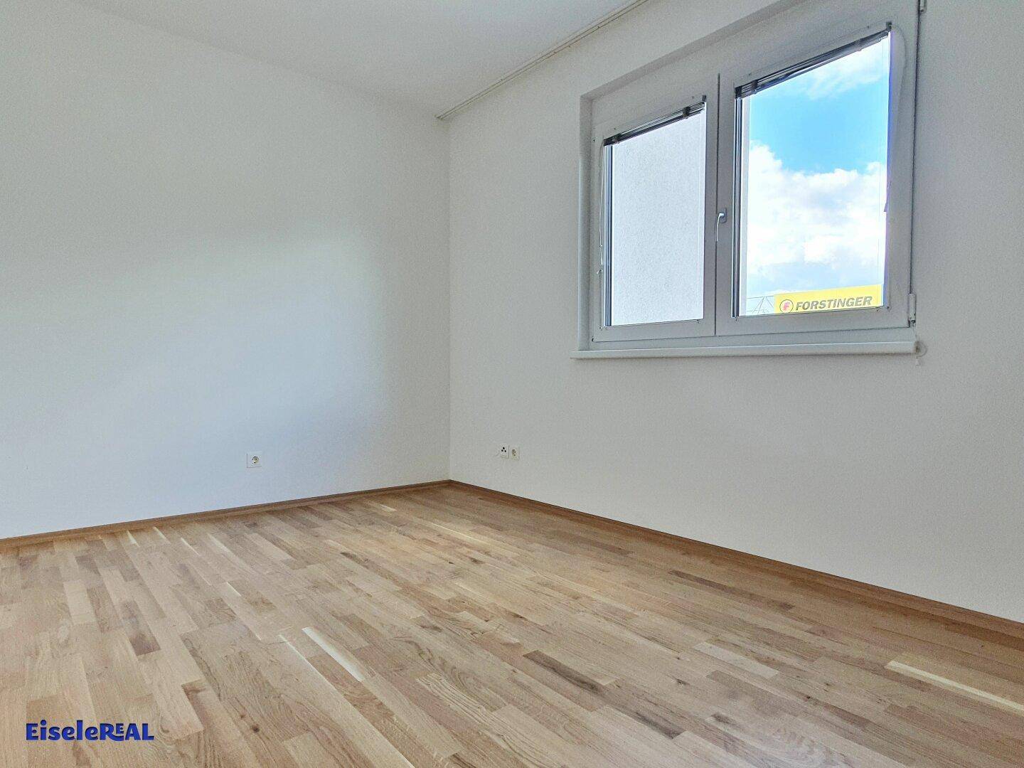 Geräumiges Schlafzimmer mit Parkettboden und großem Fenster mit Blick ins Freie.