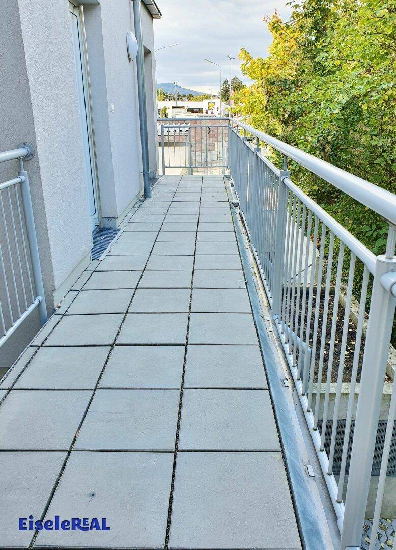 Langer, gefliester Balkon mit Metallgeländer und Blick auf die Umgebung.