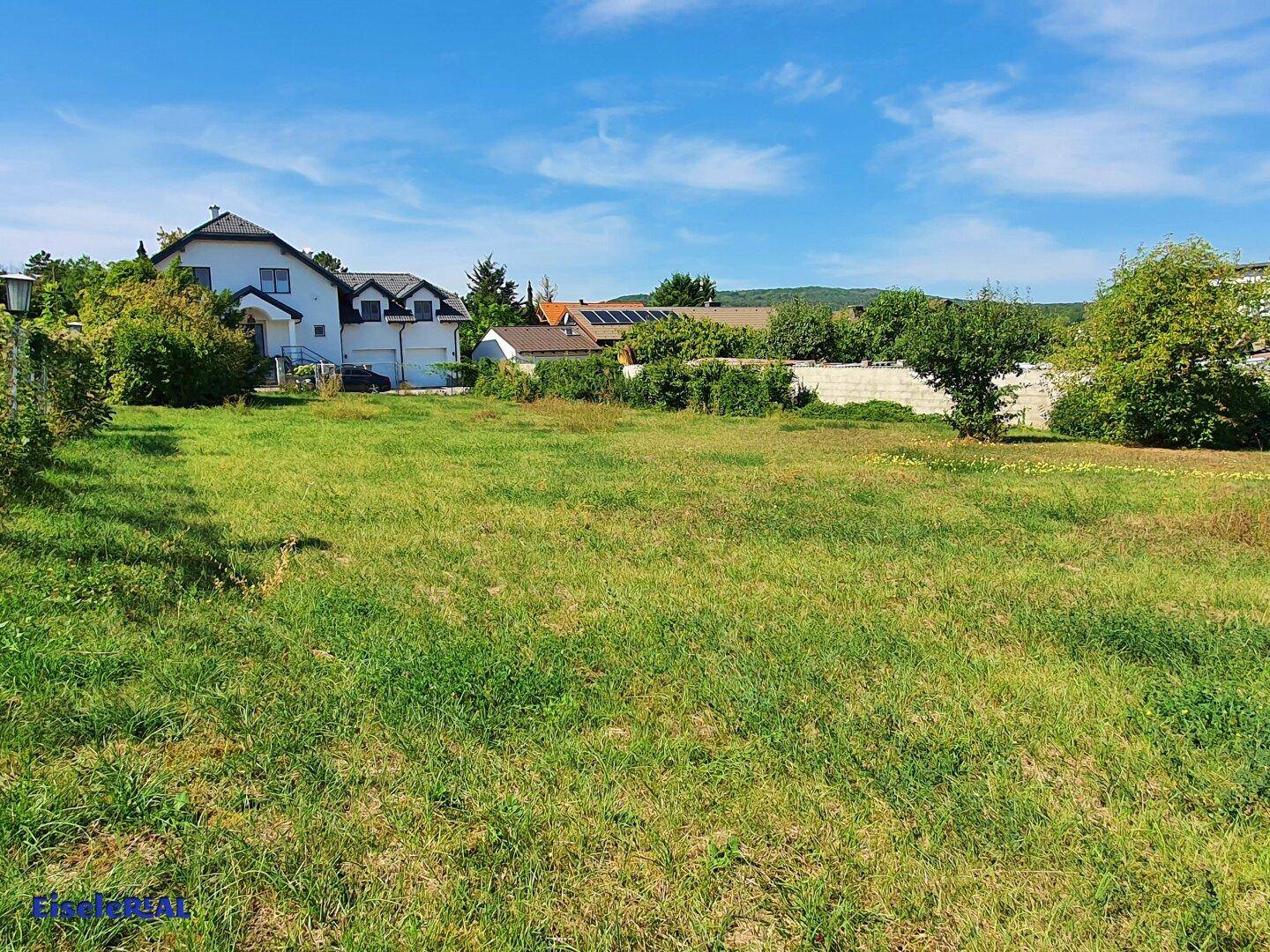 Sonniges Grundstück mit weitem Blick auf die Nachbarschaft und grüne Hügel im Hintergrund.