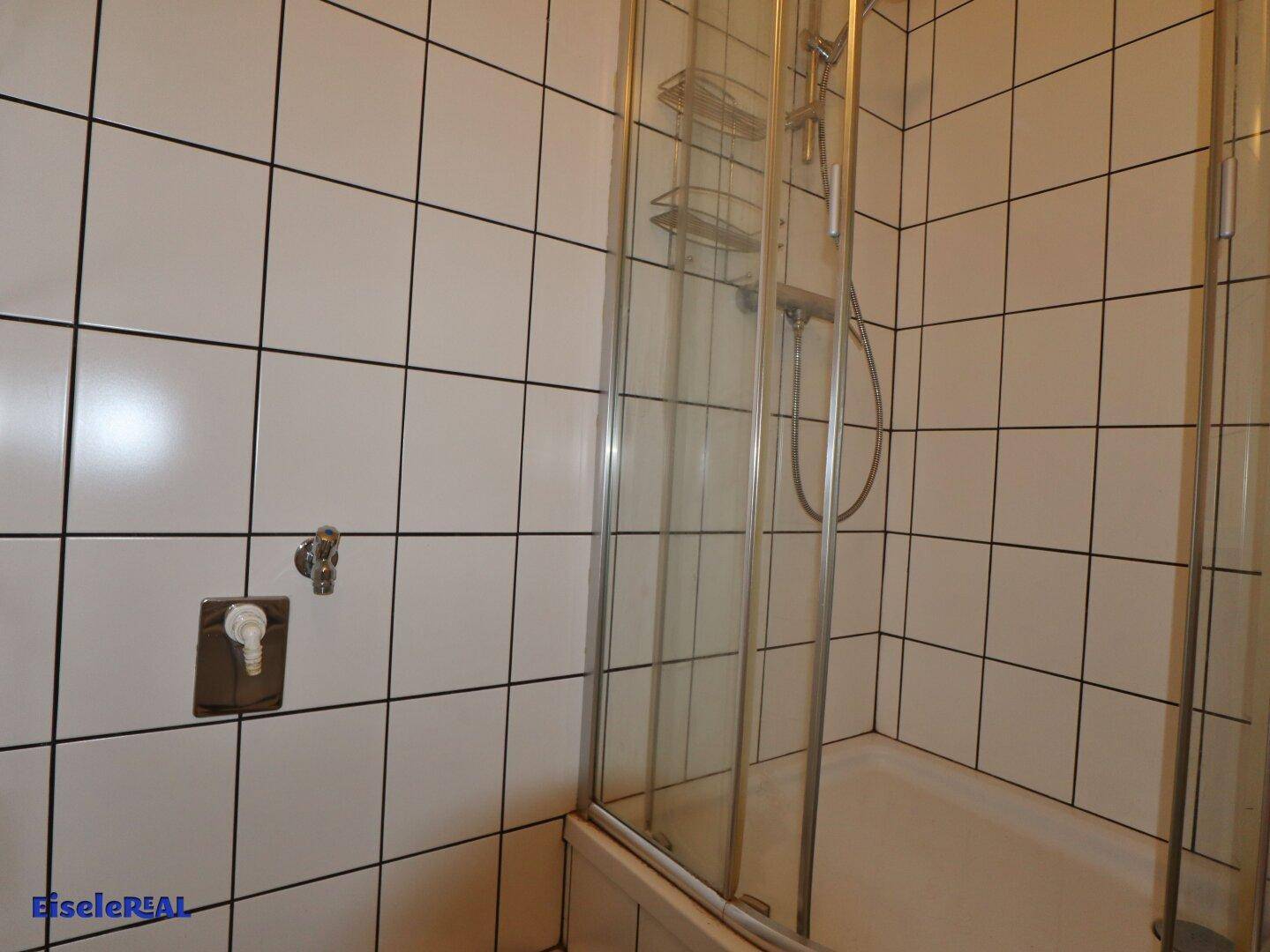 Duschbereich im Badezimmer mit weißen Fliesen und einer transparenten Duschkabine.