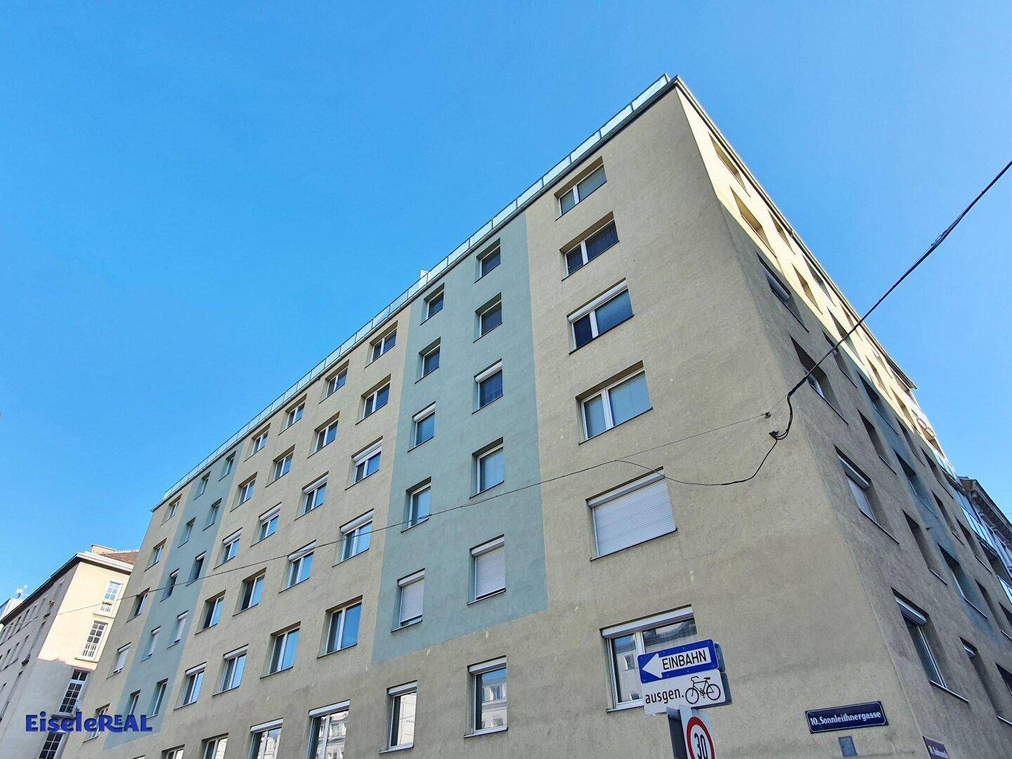 Mehrstöckiges Wohngebäude mit hellblauer und beiger Fassade unter klarem blauem Himmel.