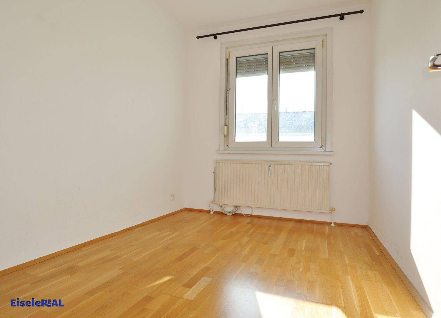 Helles Schlafzimmer mit Parkettboden und Fenster mit Rollläden, das viel Tageslicht bietet.