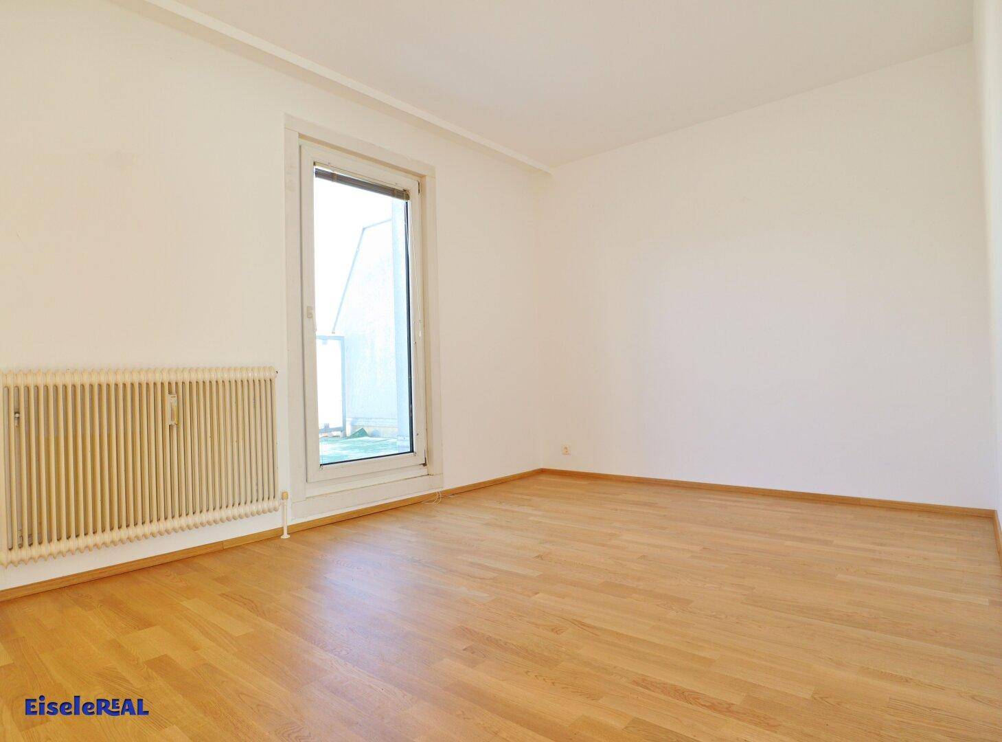 Helles Schlafzimmer mit Parkettboden und einer großen Tür, die zu einem Außenbereich führt.