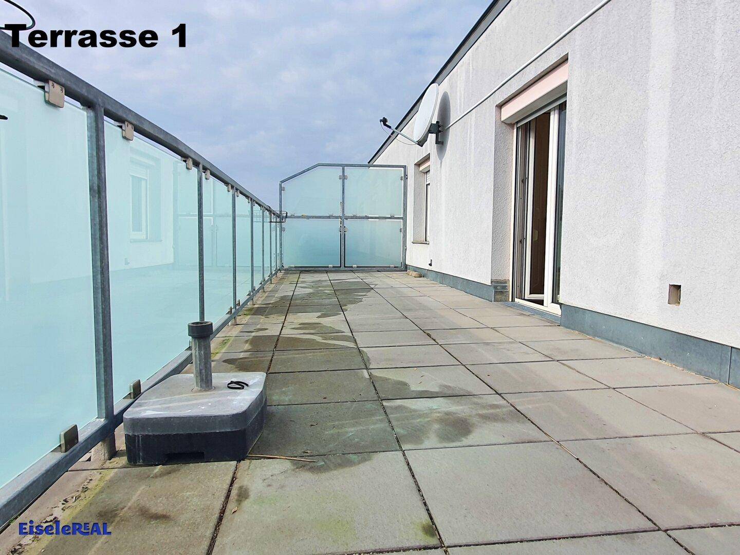 Große, geflieste Dachterrasse mit Glasgeländer und Blick auf die umliegenden Gebäude.