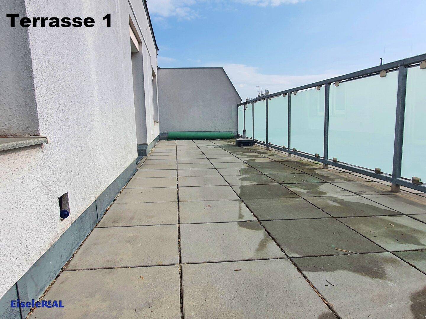 Weitläufige Dachterrasse mit grauen Fliesen und modernem Glasgeländer, ideal für Entspannung im Freien.