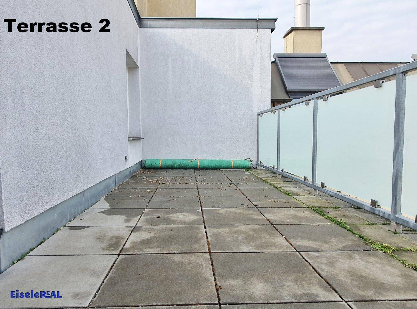 Geräumige Dachterrasse mit grauen Fliesen und Glasgeländer, bietet Platz für Outdoor-Aktivitäten.