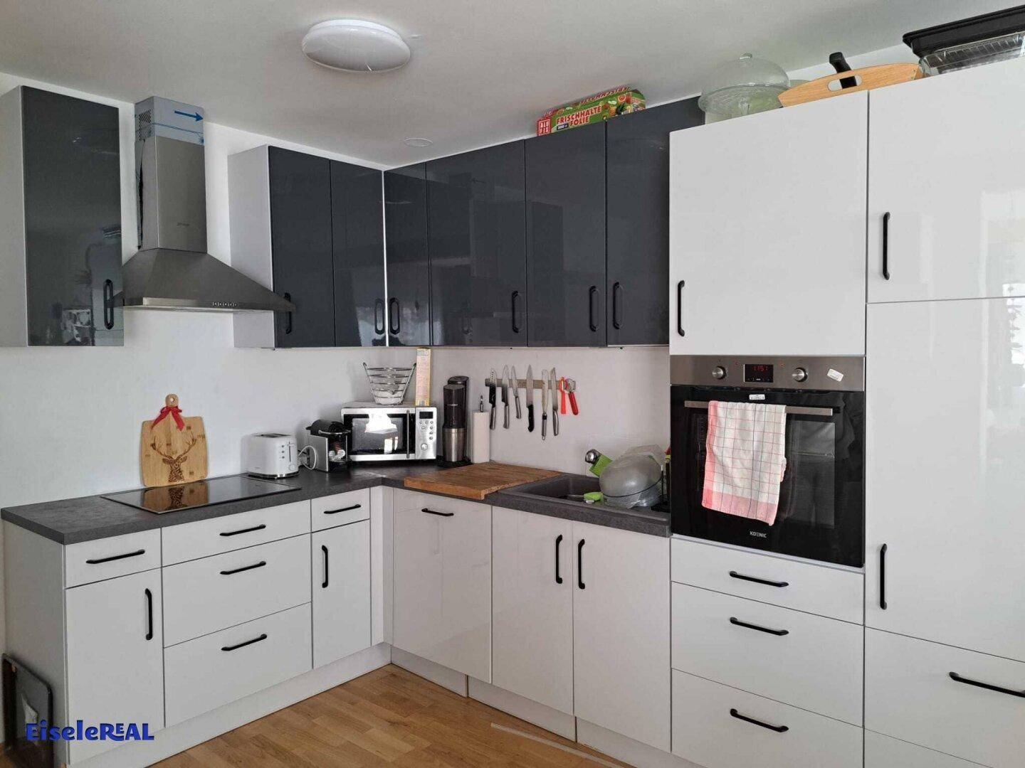 Moderne Küche mit weißen und grauen Hochglanzfronten, Einbaugeräten und Holzfußboden.
