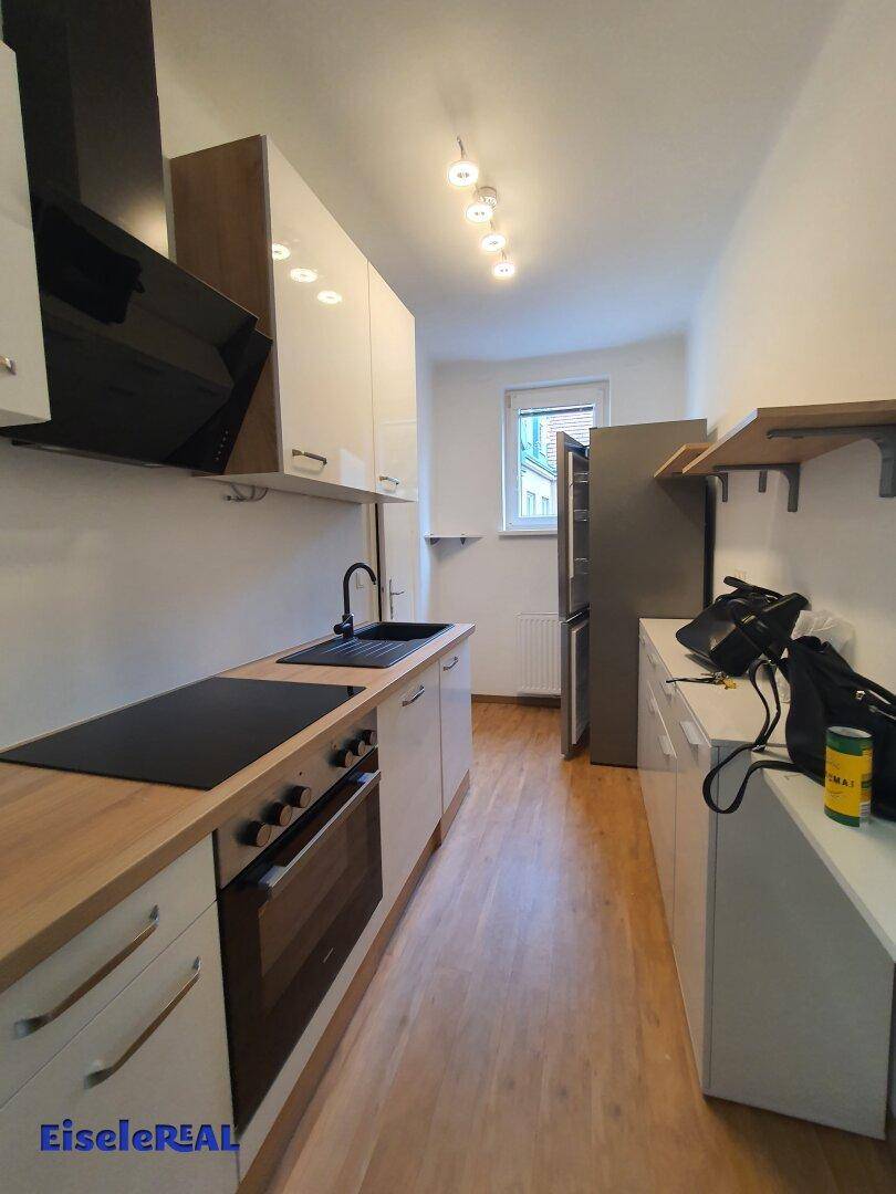 Moderne Küche mit weißen Schränken, Holzarbeitsplatte, Induktionskochfeld und Kühlschrank.
