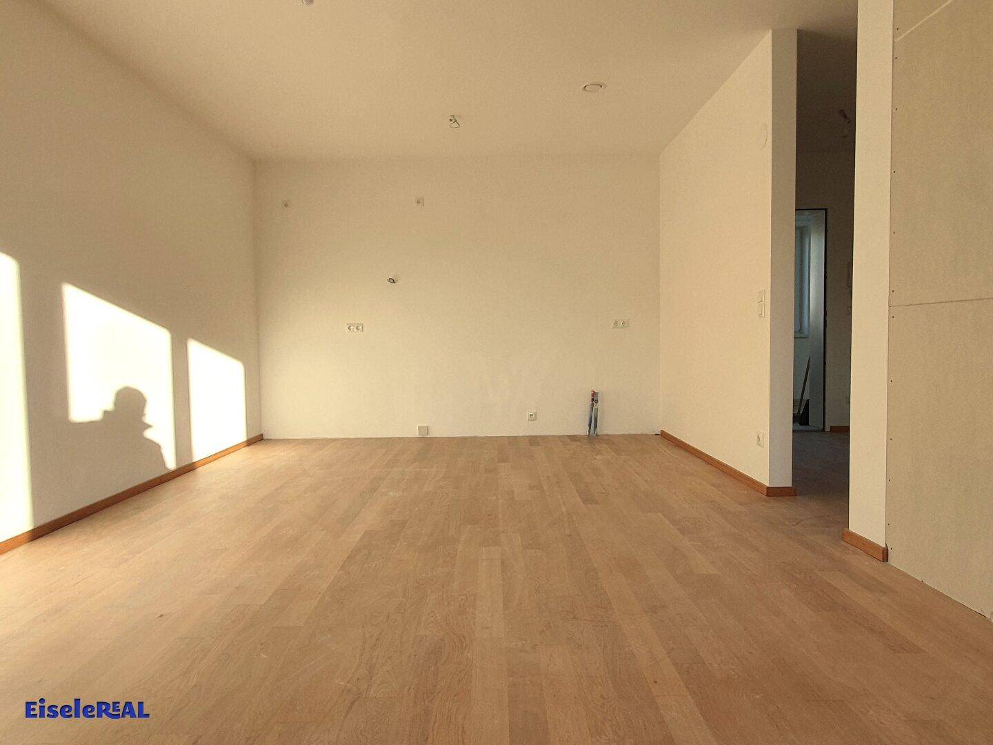 Geräumiger, unmöblierter Raum mit hellem Holzboden und viel natürlichem Lichteinfall durch Fenster.