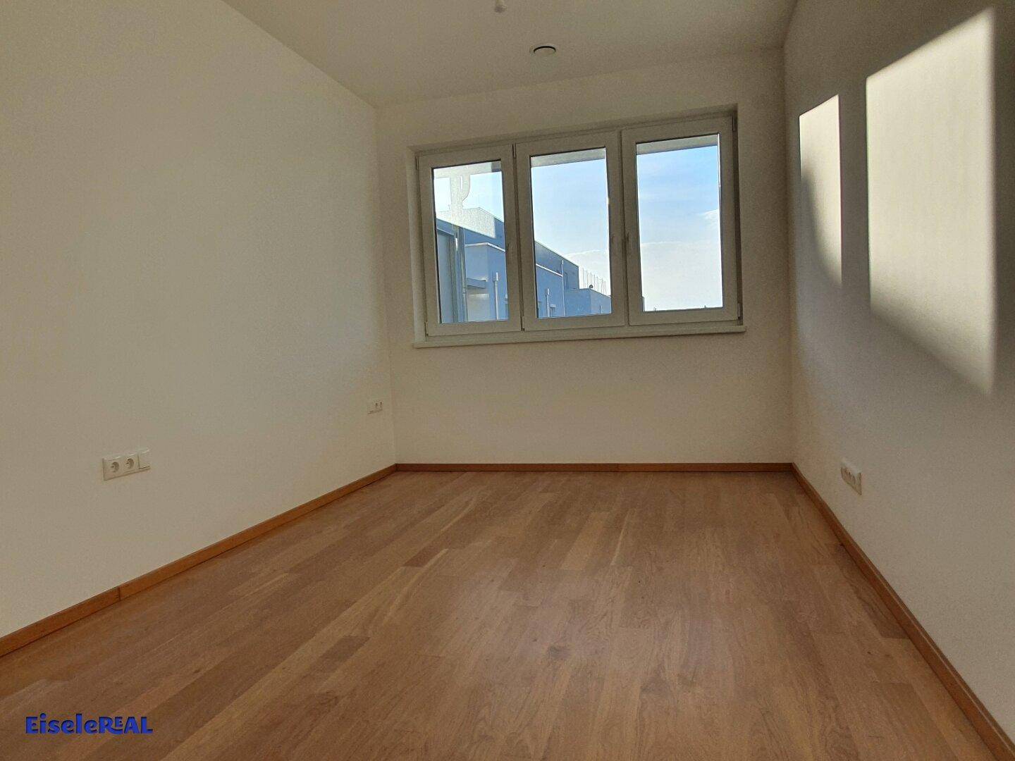 Unmöbliertes Schlafzimmer mit Holzboden und Fenster, das von der Sonne durchflutet wird.