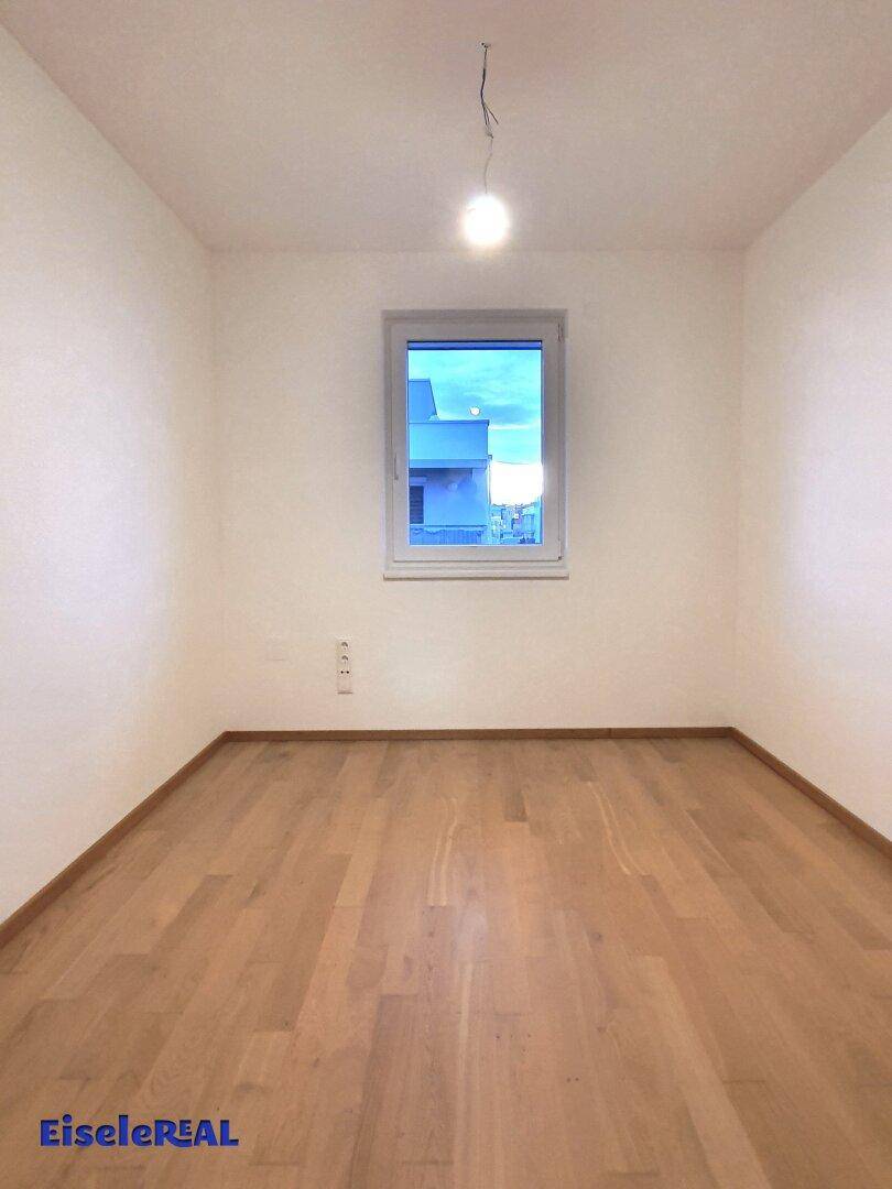 Leeres Zimmer mit Parkettboden und einem Fenster, ideal als Schlaf- oder Arbeitszimmer.
