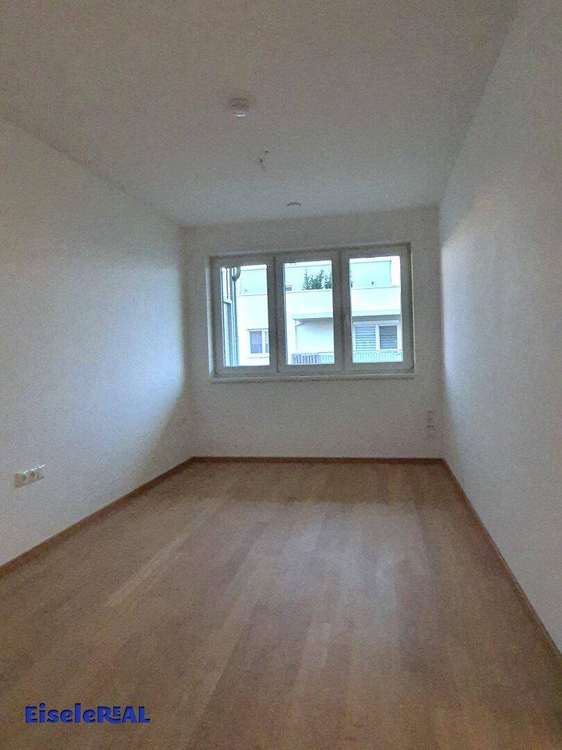 Helles, leeres Zimmer mit Parkettboden und mehreren Fenstern für viel Tageslicht.