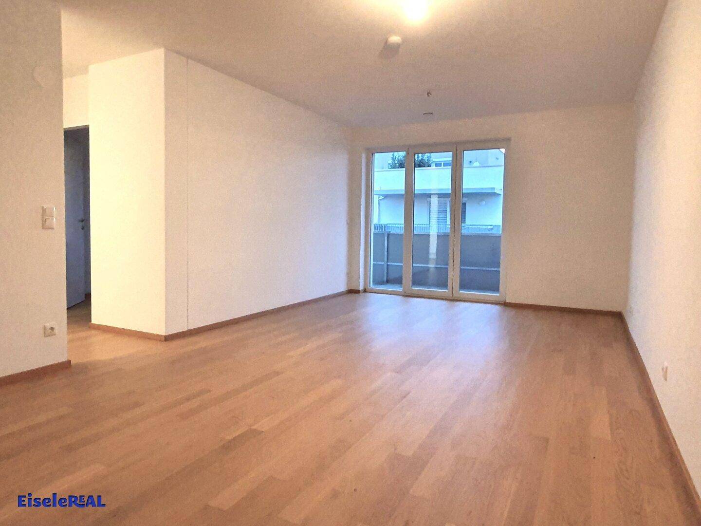 Heller, leerer Wohnbereich mit Parkettboden und Zugang zu einem Balkon oder einer Terrasse.