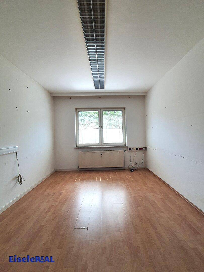 Leerer Raum mit Laminatboden, einem Fenster und Heizkörper.