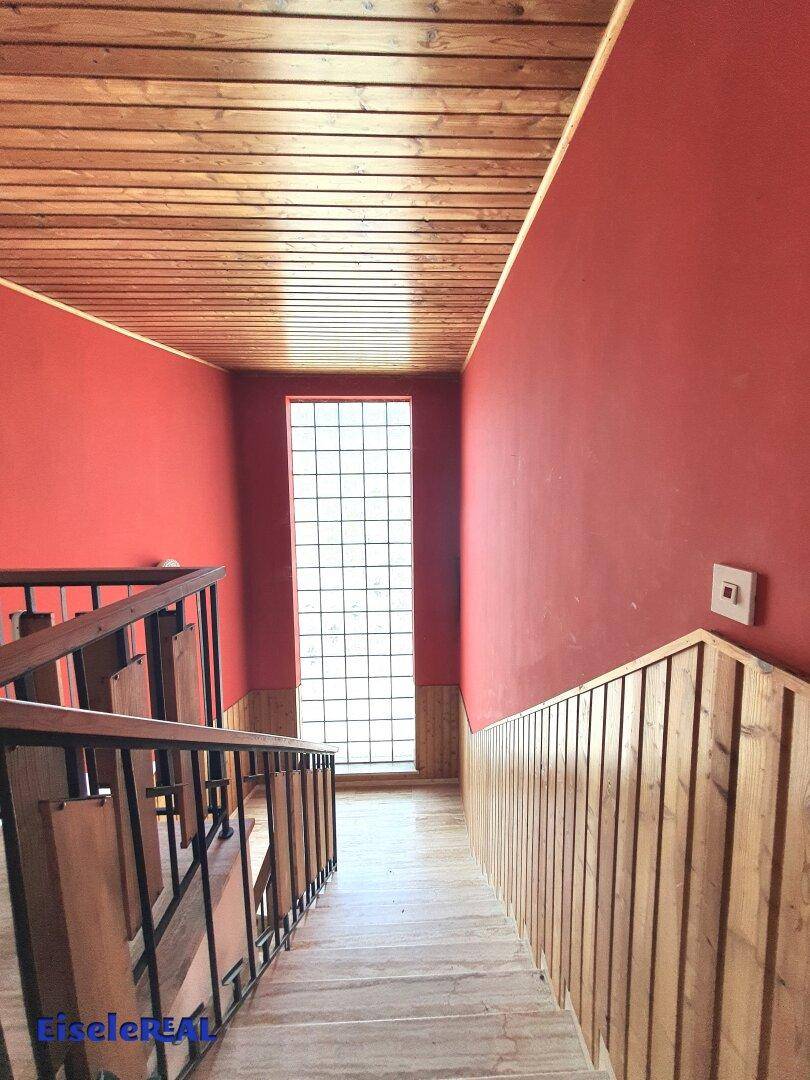 Treppenhaus mit Holzverkleidung, roten Wänden und einem hohen Glasbausteinfenster.