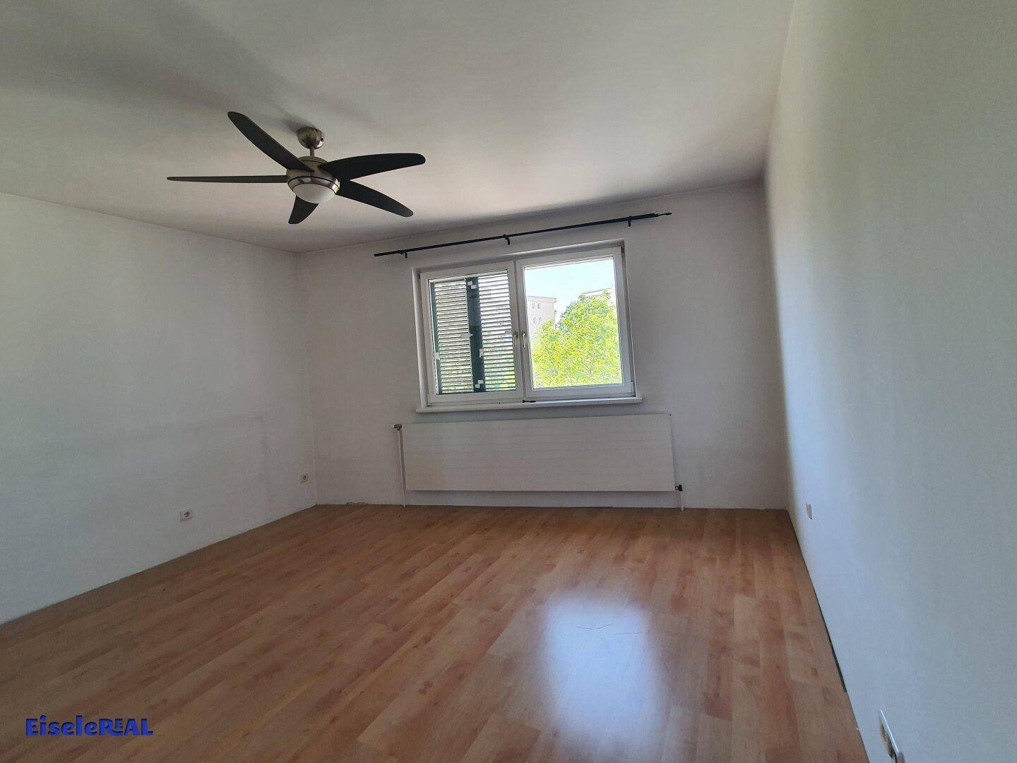 Helles Zimmer mit Laminatboden, Deckenventilator und Blick ins Grüne.