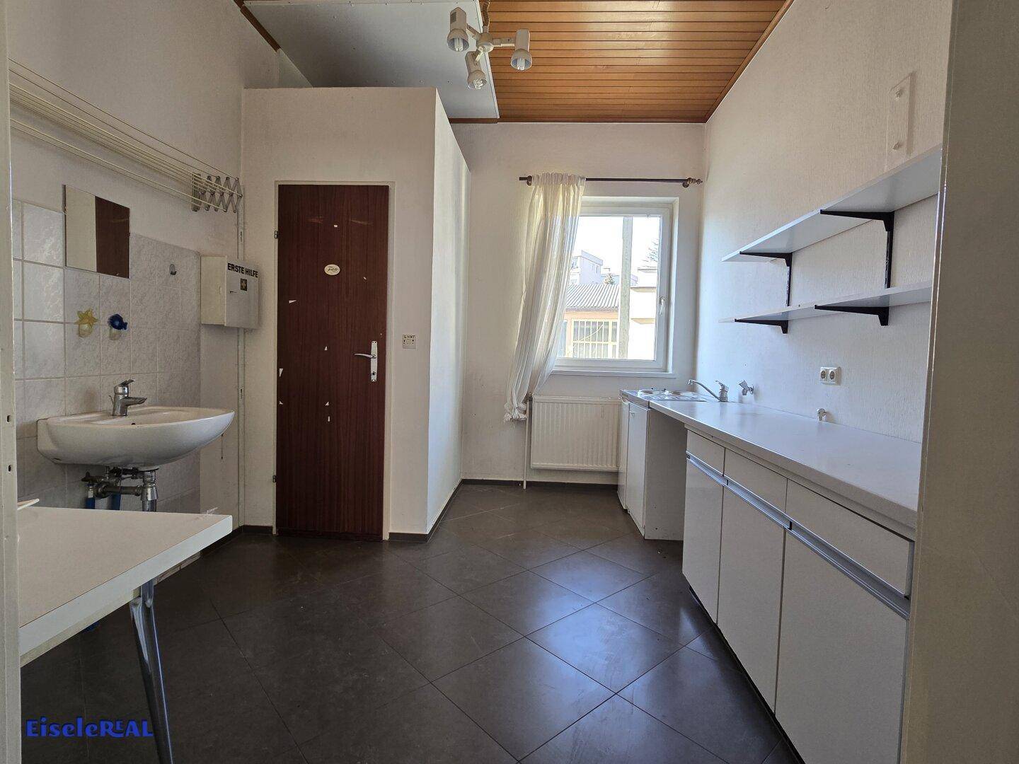 Einfache Küchenzeile mit Spülbecken, Unterschränken und Holzdecke in einem funktionalen Raum.