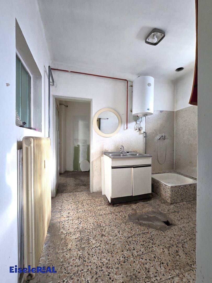 Funktionales Badezimmer mit Waschbecken, Boiler und kleiner Duschwanne, in renovierungsbedürftigem Zustand.