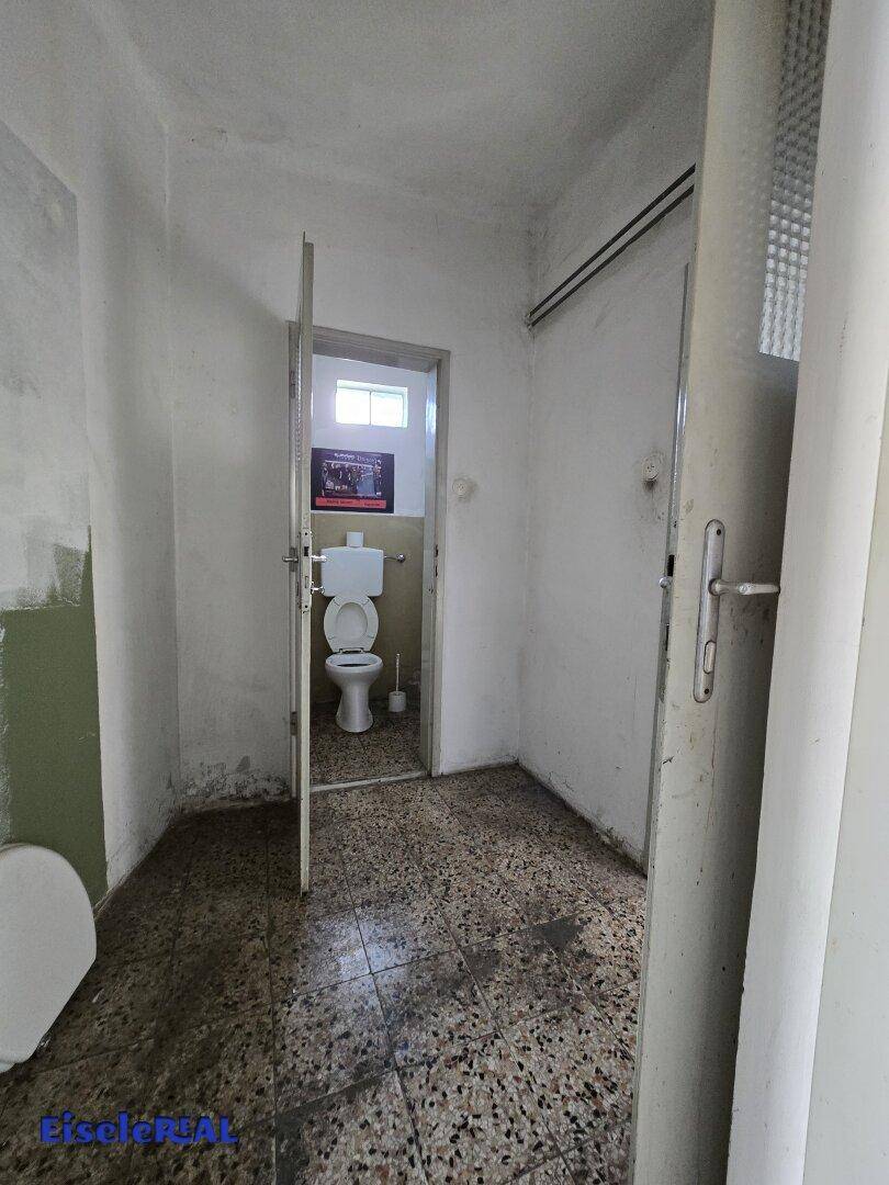 Schmaler Flur mit Fliesenboden, der zu einer separaten Toilette führt, in einfachem Zustand.