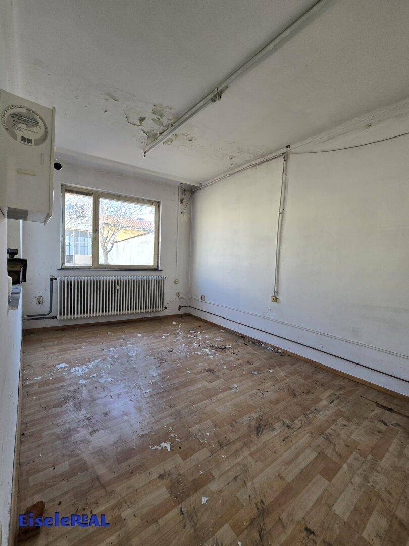 Leerer Raum mit Parkettboden, Fenster und Heizkörper, der Renovierung benötigt.