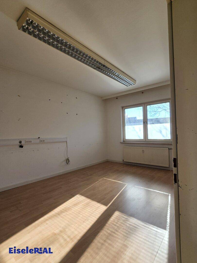 Leerer Raum mit Laminatboden, Fenster und Heizkörper, gut beleuchtet durch Tageslicht.