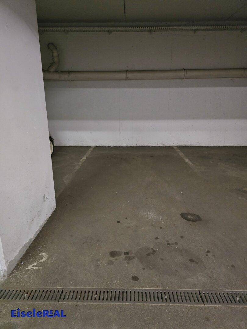 Leerer Tiefgaragenstellplatz mit Betonboden und Markierungen.