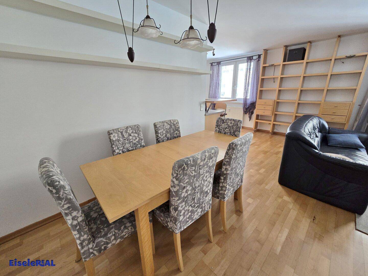 Essbereich mit Holztisch, Stühlen und einem Sofa, verbunden mit dem Wohnzimmer.