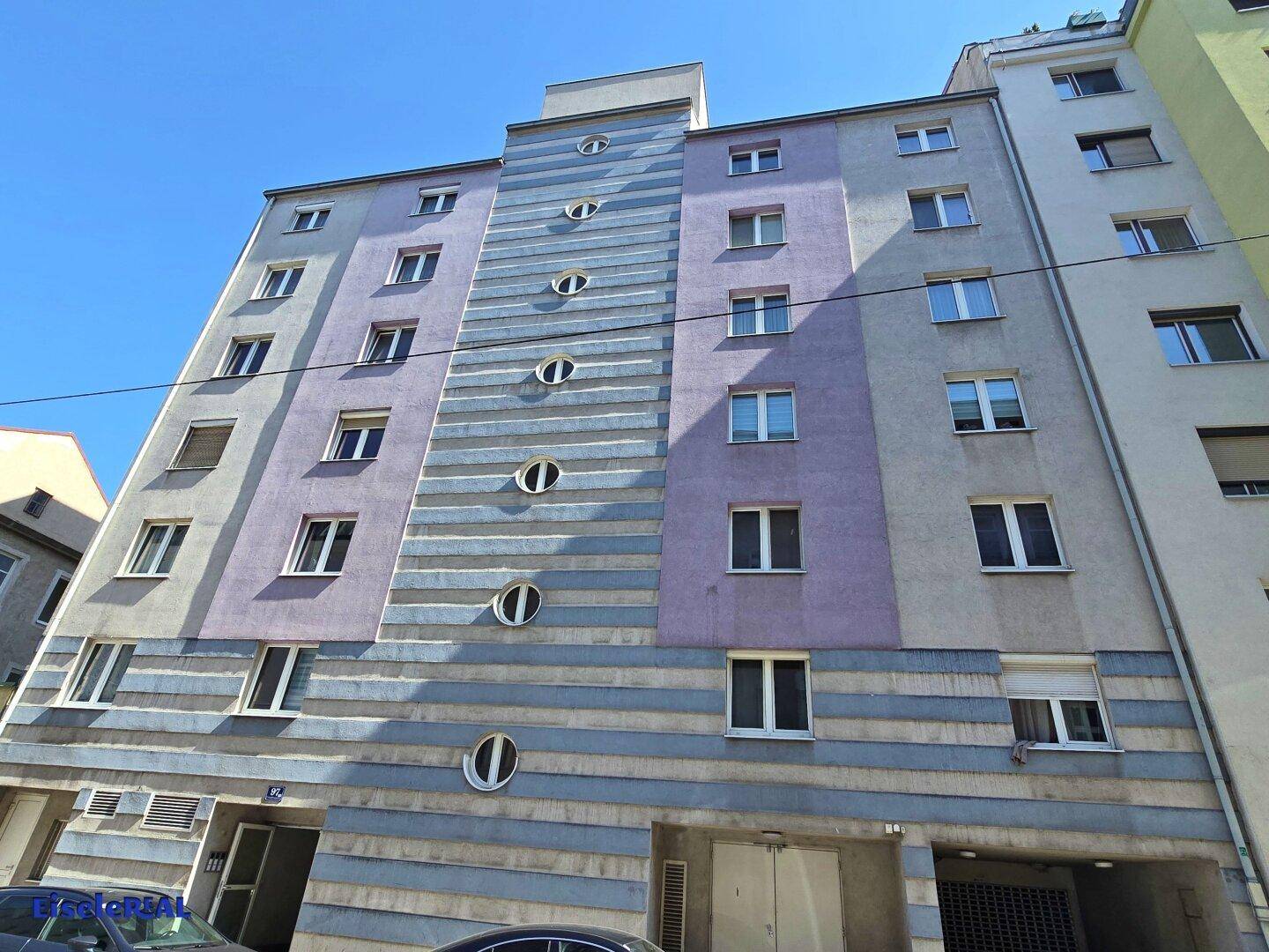 Ansicht der farbigen Fassade eines Wohngebäudes mit runden und rechteckigen Fenstern.