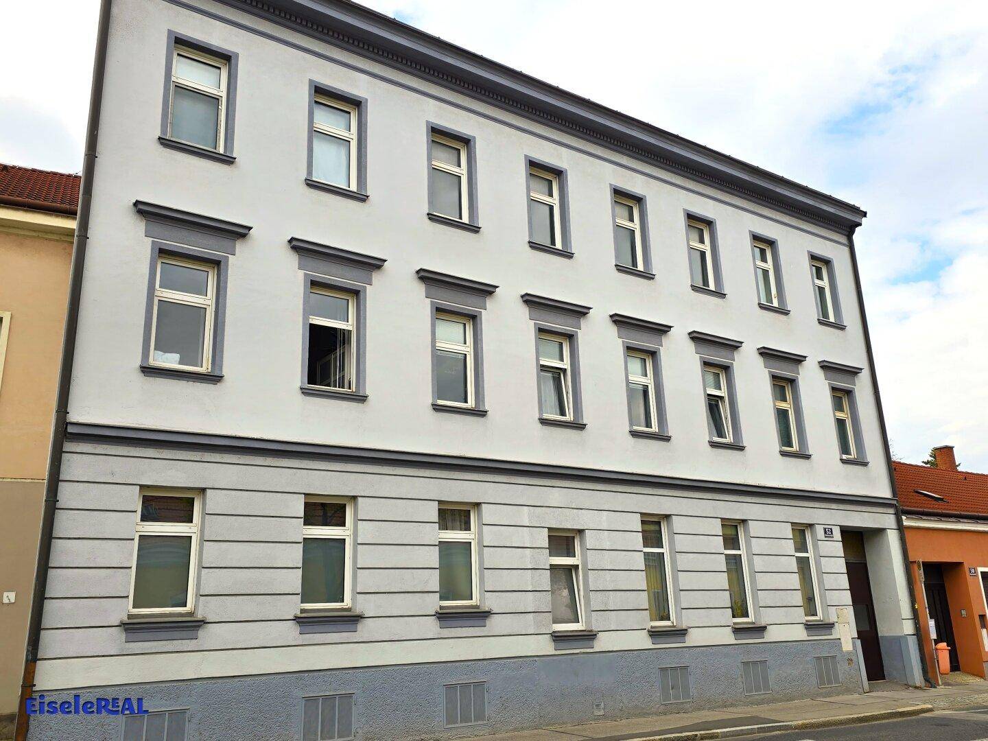 Seitenansicht der Gebäudefassade mit Reihen von Fenstern und einem Eingangsbereich auf der rechten Seite.