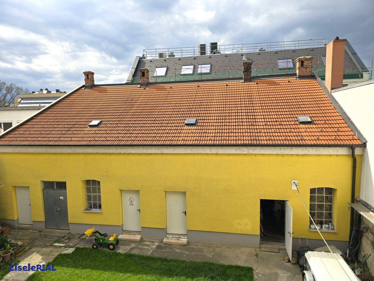Dachansicht des gelben Nebengebäudes mit Ziegeln und Schornsteinen, im Hintergrund weitere Gebäude.