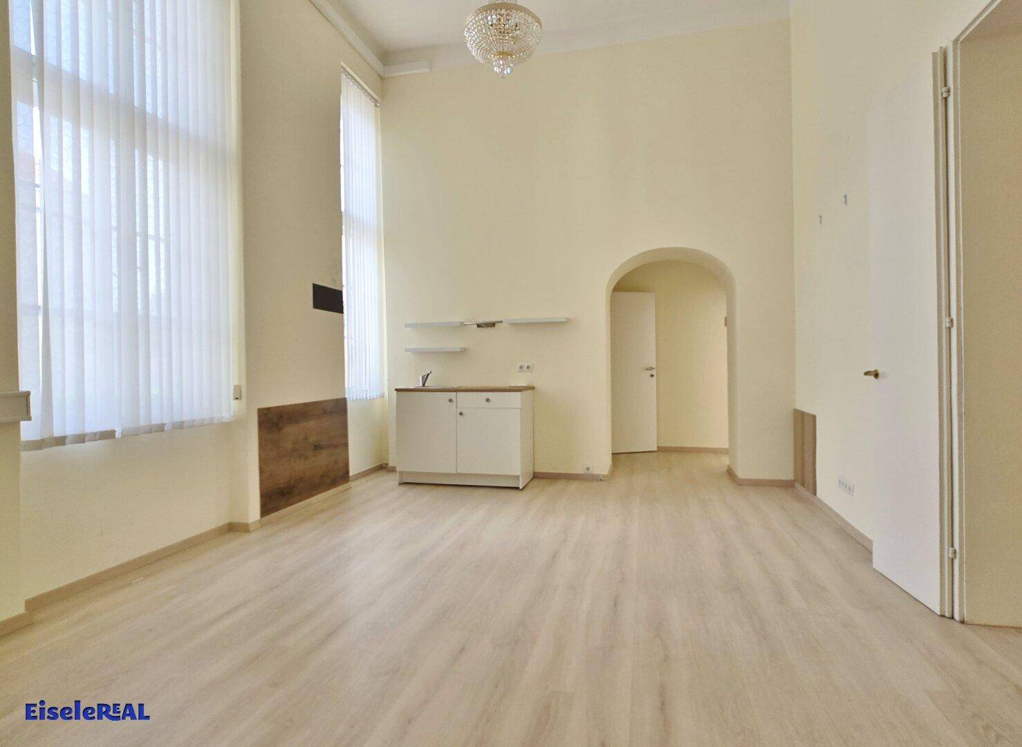 Heller Raum mit Laminatboden, hohen Decken und einem kleinen Küchenschrank unter einem dekorativen Bogen.