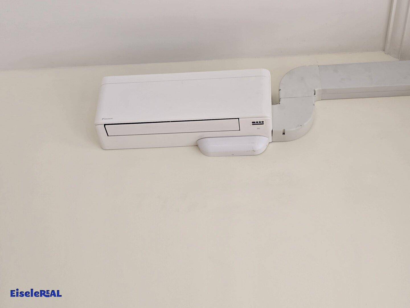 Nahaufnahme einer modernen Klimaanlage, die an der Wand in einem hellen, neutralen Raum montiert ist.