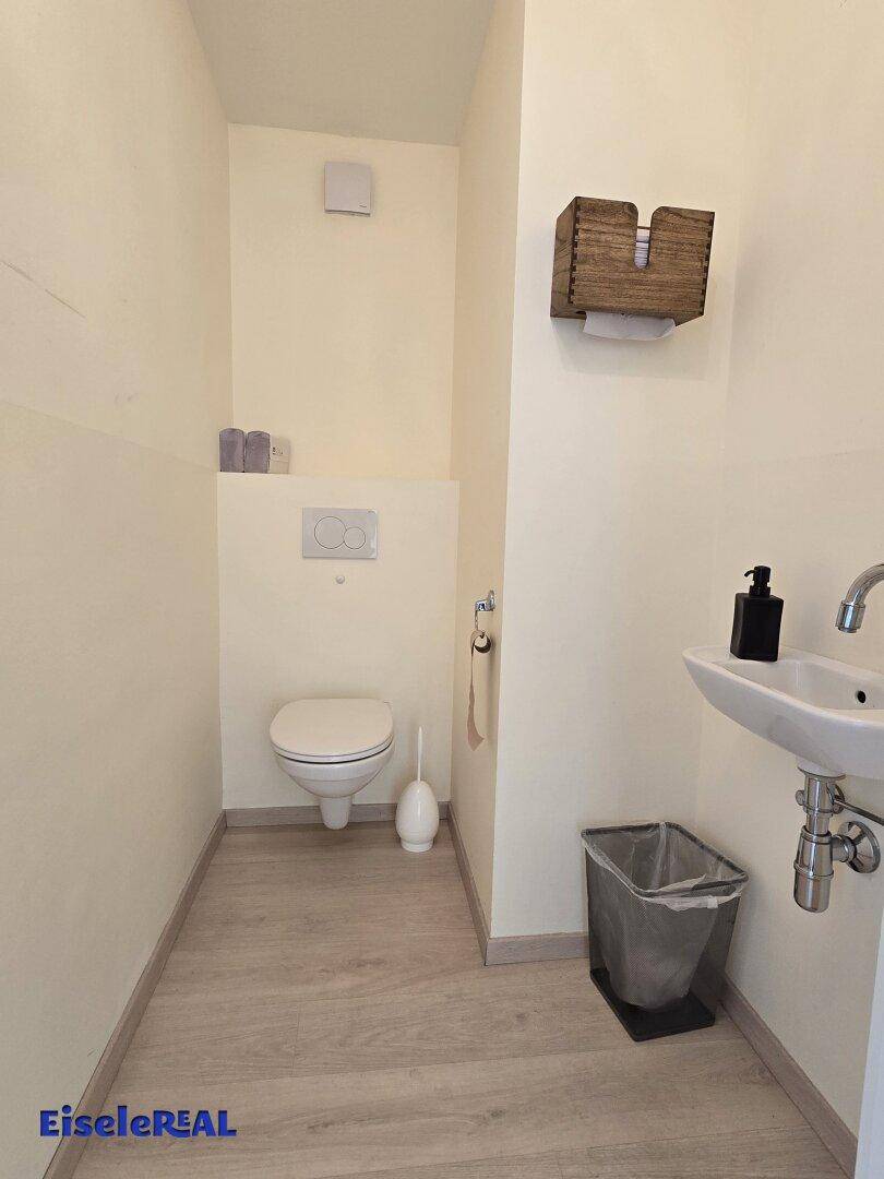 Kleine Gästetoilette mit wandhängendem WC, Waschbecken und Holzoptik-Boden in einem gepflegten Zustand.