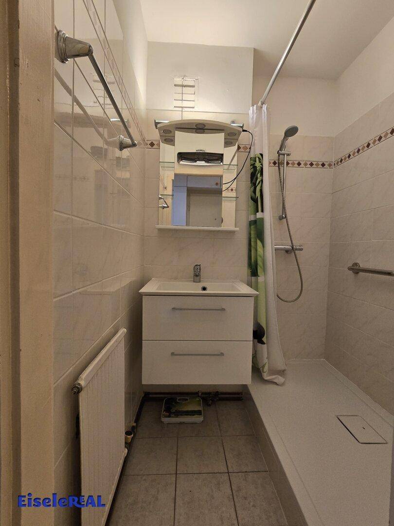 Helles Badezimmer mit Dusche, Waschbecken und Spiegel.