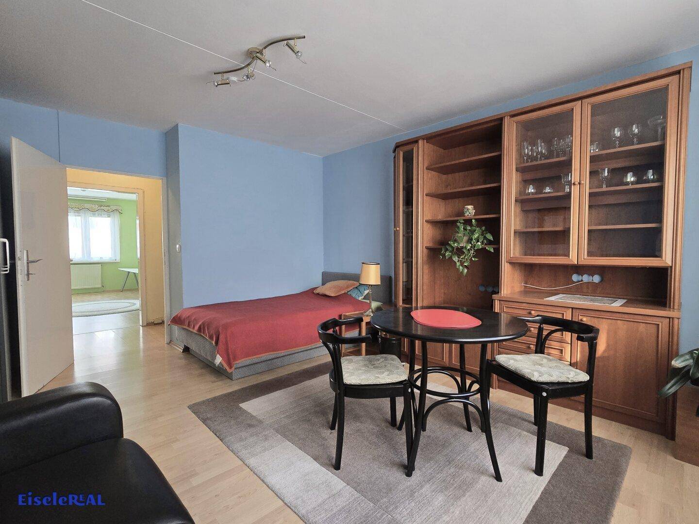 Heller Wohnbereich mit Holzboden, blauen Wänden und Zugang zu einem weiteren Zimmer.