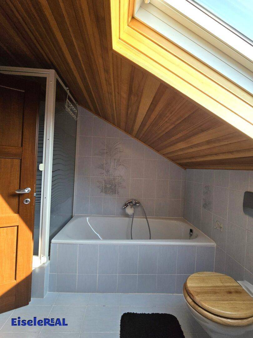 Badezimmer mit Badewanne, Duschbereich und Holzdecke unter der Dachschräge.