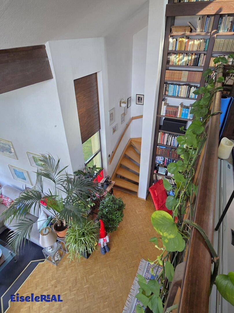 Treppenaufgang und Bücherregal in einem hellen, offenen Wohnbereich mit Galerie.