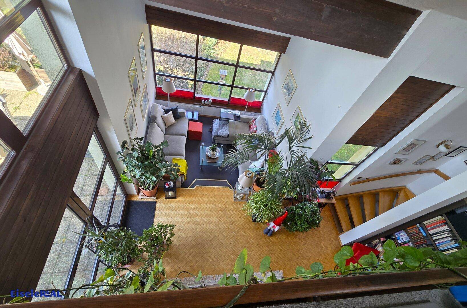 Weitläufiger Blick von der Galerie auf das Wohnzimmer mit großen Fenstern und viel Grün.