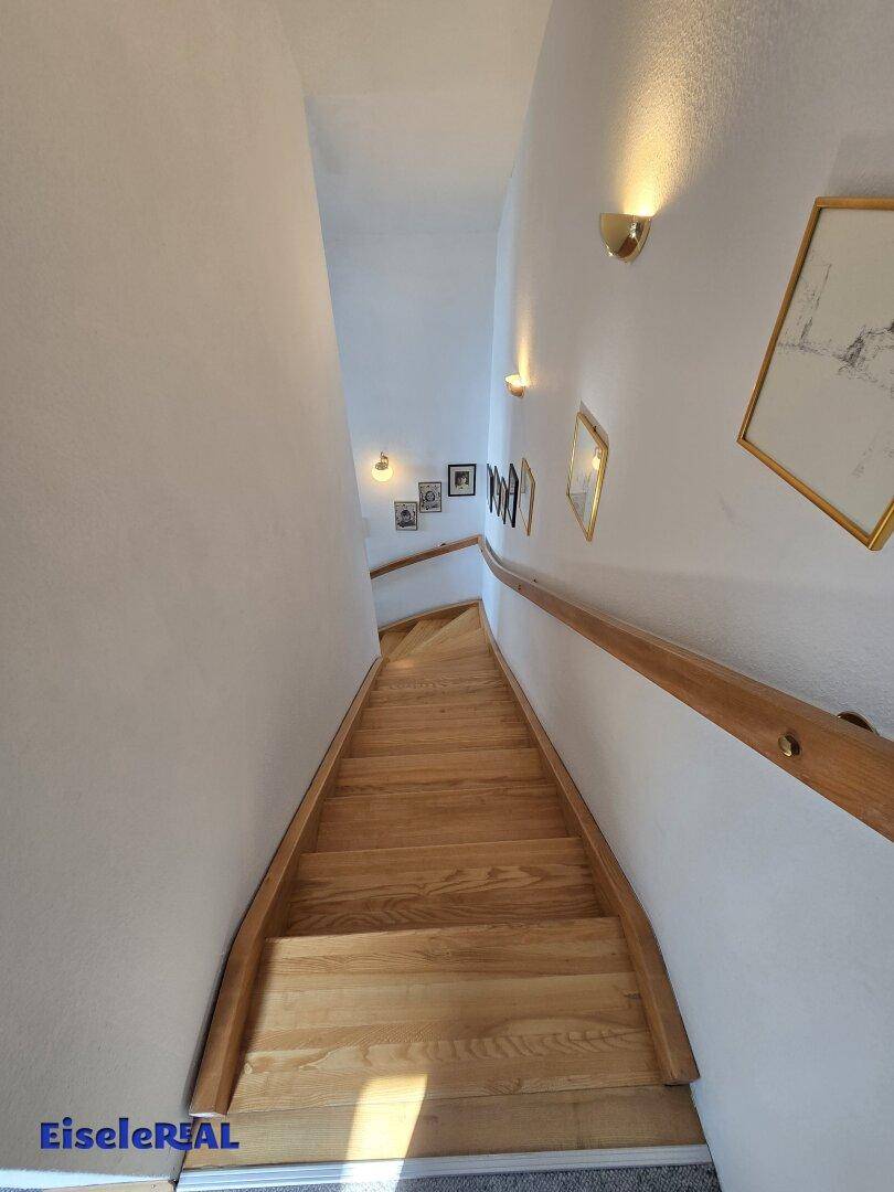 Heller Holztreppenaufgang mit Handlauf und Wandbeleuchtung.