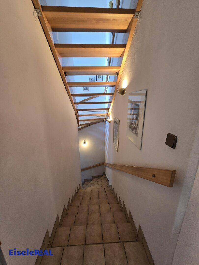 Treppenhaus mit Holzstufen und Fliesenboden im unteren Bereich.