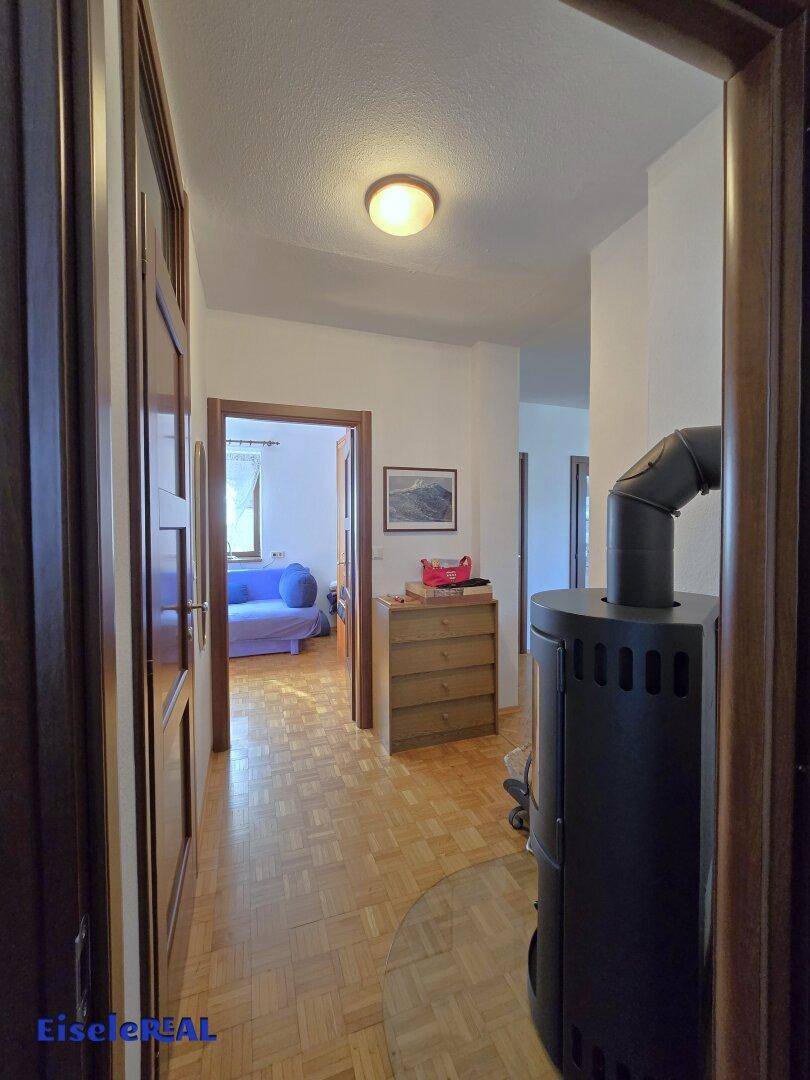 Heller Flur mit Holzofen und Blick in ein angrenzendes Zimmer.