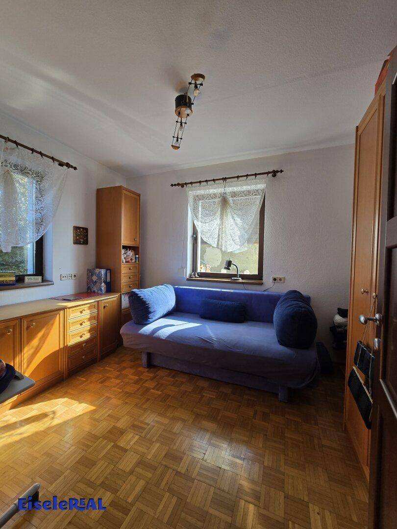 Gemütliches Schlafzimmer mit Parkettboden, Fenstern und einem blauen Sofa.