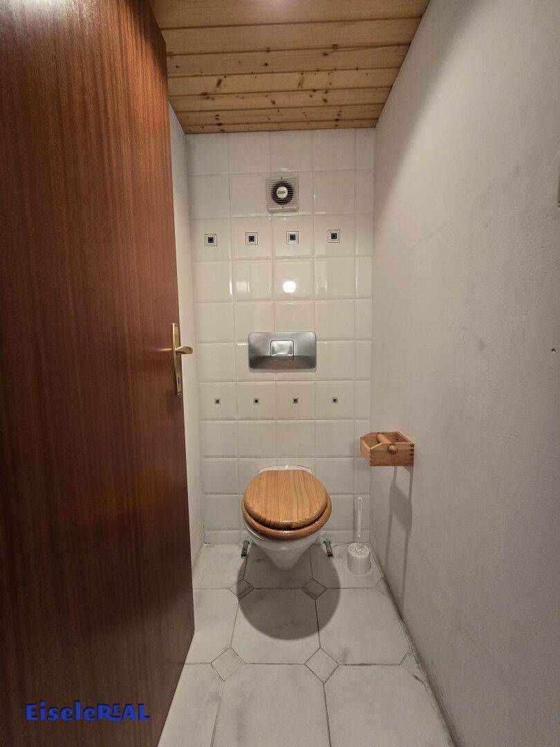 Kleines Gäste-WC im Keller mit weißen Fliesen und Holz-WC-Sitz.